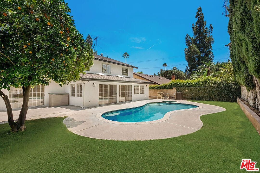 Backyard pool area with a small grass lawn and orange tree