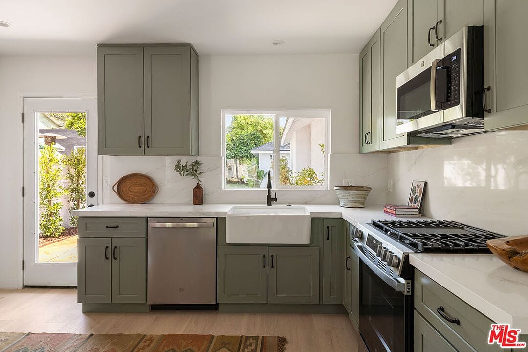 Kitchen sink area with sage green cabinets, white countertops, and window
