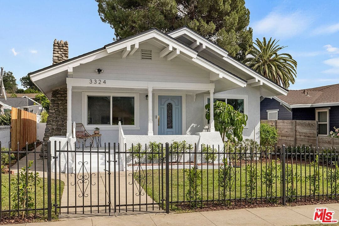 Front view of the light grey bungalow with a black metal fence and stone chimney