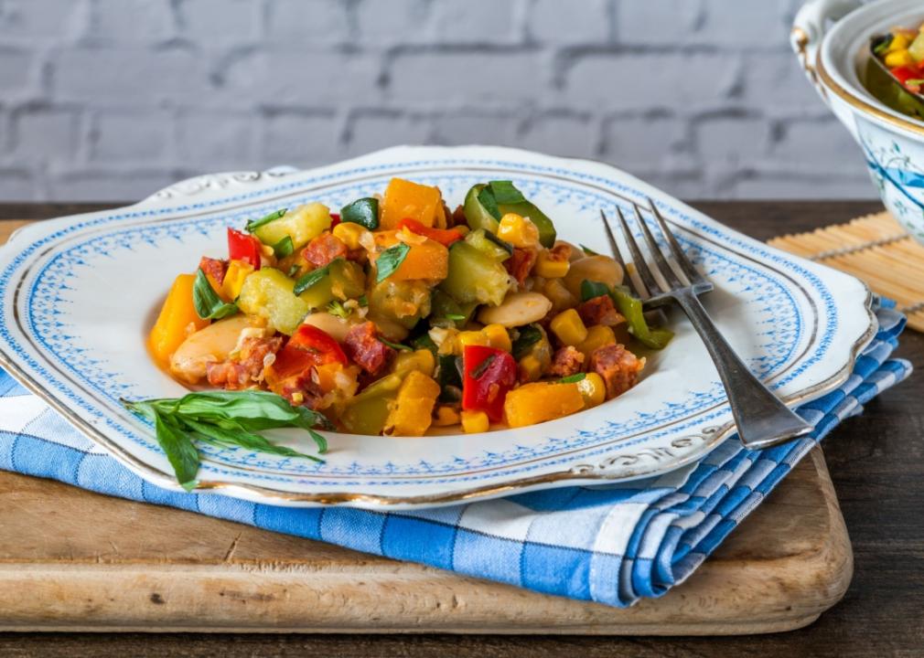 Succotash A plate of vegetables, butter beans, butternut squash, sweetcorn and pieces of sausage. The plate sits on top of blue kitchen towel and cutting wooden board.