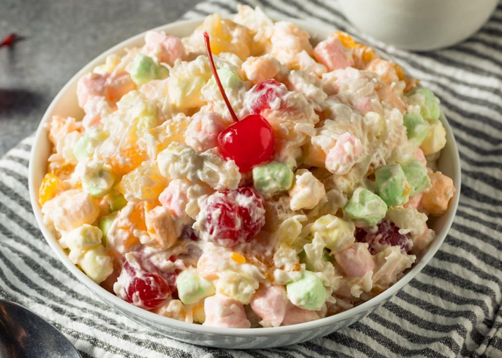 Ambrosia salad Various types of cut-up fruit in the bowl, including green grapes, red grapes, strawberries, and marshmallows with a cherry on top.