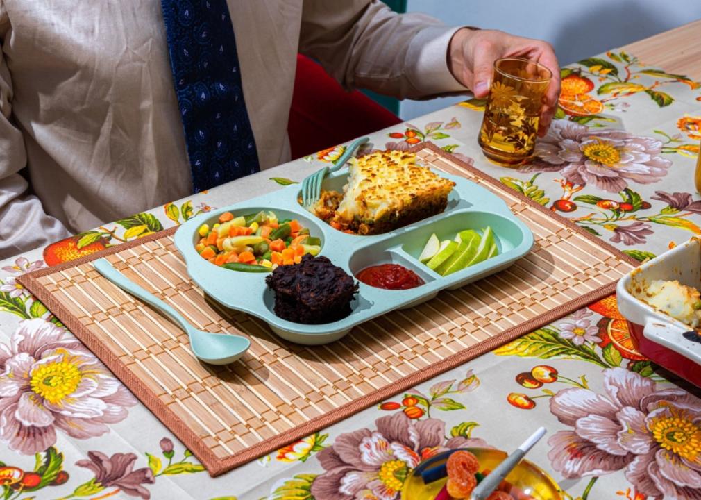 TV dinners A man sitting in front of the plastic blue tray with a meal compartmentalized into sections with mashed potatoes and ground meat, sliced green apple, mixed veggies and a muffin.