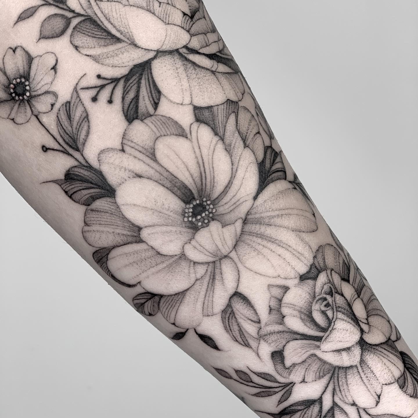Delicate botanical artistry blooms across this arm in exquisite black and gray, where peonies and roses intertwine with masterful dotwork details that catch the light beautifully. The seamless flow from larger statement flowers to smaller accent blooms creates such gorgeous visual depth and movement 🌸 Pure floral elegance with that timeless, vintage-inspired aesthetic that never goes out of style.