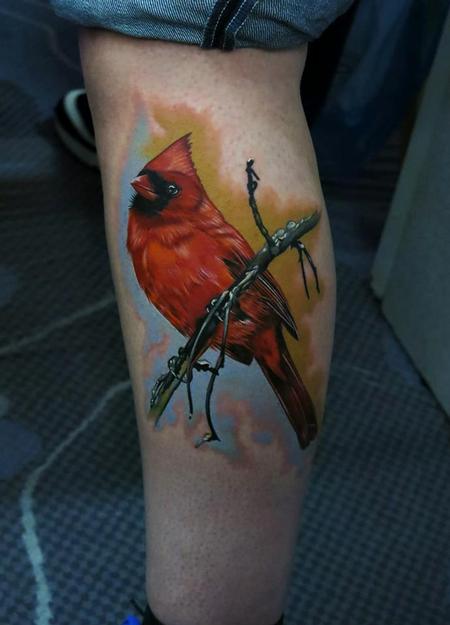 Perched gracefully on a branch against a dreamy sunset backdrop, this cardinal tattoo showcases incredible realism and artistic depth 🐦 The rich crimson plumage contrasts beautifully with the soft watercolor-style background, while the detailed branch work adds perfect natural framing. Positioned on the calf, this piece transforms the leg into a living canvas that celebrates both wildlife beauty and masterful tattoo artistry.
