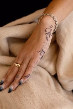 Delicate script flows like a gentle river down this hand, creating an elegant pathway of words that transforms the skin into living poetry. The graceful lettering paired with dainty chain jewelry creates a cohesive aesthetic that's both romantic and refined ✨