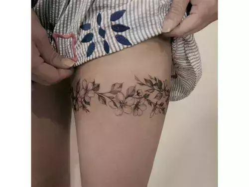 Delicate botanical artistry wraps around the thigh like nature's own jewelry, creating an enchanting floral band that celebrates the feminine form. The intricate linework and organic flow of leaves and blossoms transforms this placement into a living garden, perfectly complementing the body's natural curves. 🌿