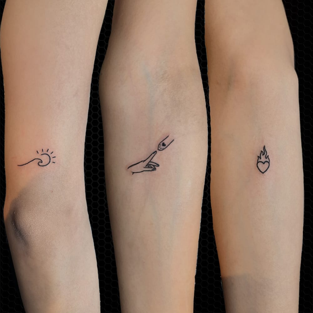 Delicate line work transforms three forearms into a canvas of elemental storytelling ✨ From left to right, a minimalist wave meets sunshine, a graceful hand holds Neptune's trident, and a sacred heart burns with eternal flame. These perfectly coordinated pieces prove that matching tattoos don't have to be identical—they just need to speak the same symbolic language of natural forces and human connection.