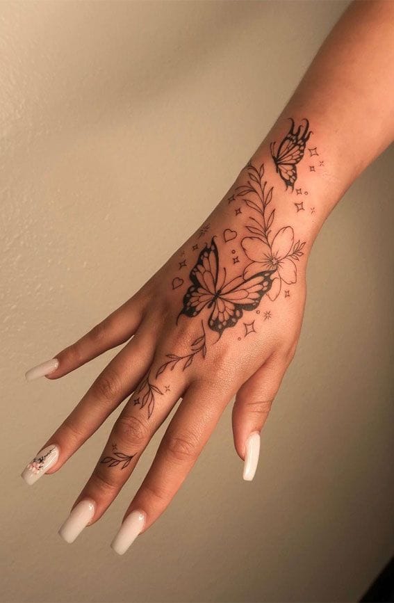 Delicate butterflies dance across skin like living art, their wings catching light as they flutter from wrist to fingertips in perfect harmony. The intricate linework weaves together florals and tiny stars, creating a whimsical garden that blooms eternally on this stunning hand placement 🦋 Pure enchantment captured in ink!