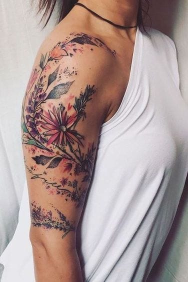 A breathtaking watercolor wildflower garden blooms across this upper arm, featuring delicate botanical elements that seem to dance with life and movement. The artist's masterful use of soft pinks, purples, and greens creates an almost painterly effect, while intricate line work adds depth and definition to each petal and leaf 🌸 This piece perfectly demonstrates how floral tattoos can be both bold and feminine, wrapping the arm like nature's own sleeve.