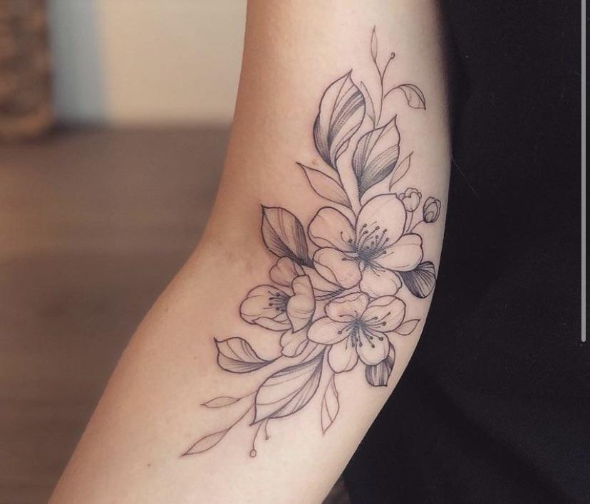 Delicate line work transforms this forearm into a botanical canvas, where cherry blossoms dance gracefully across pale skin in soft black ink. The artist's masterful shading technique brings depth to each petal while maintaining that coveted minimalist aesthetic—perfect for anyone seeking floral femininity with sophisticated restraint. 🌸