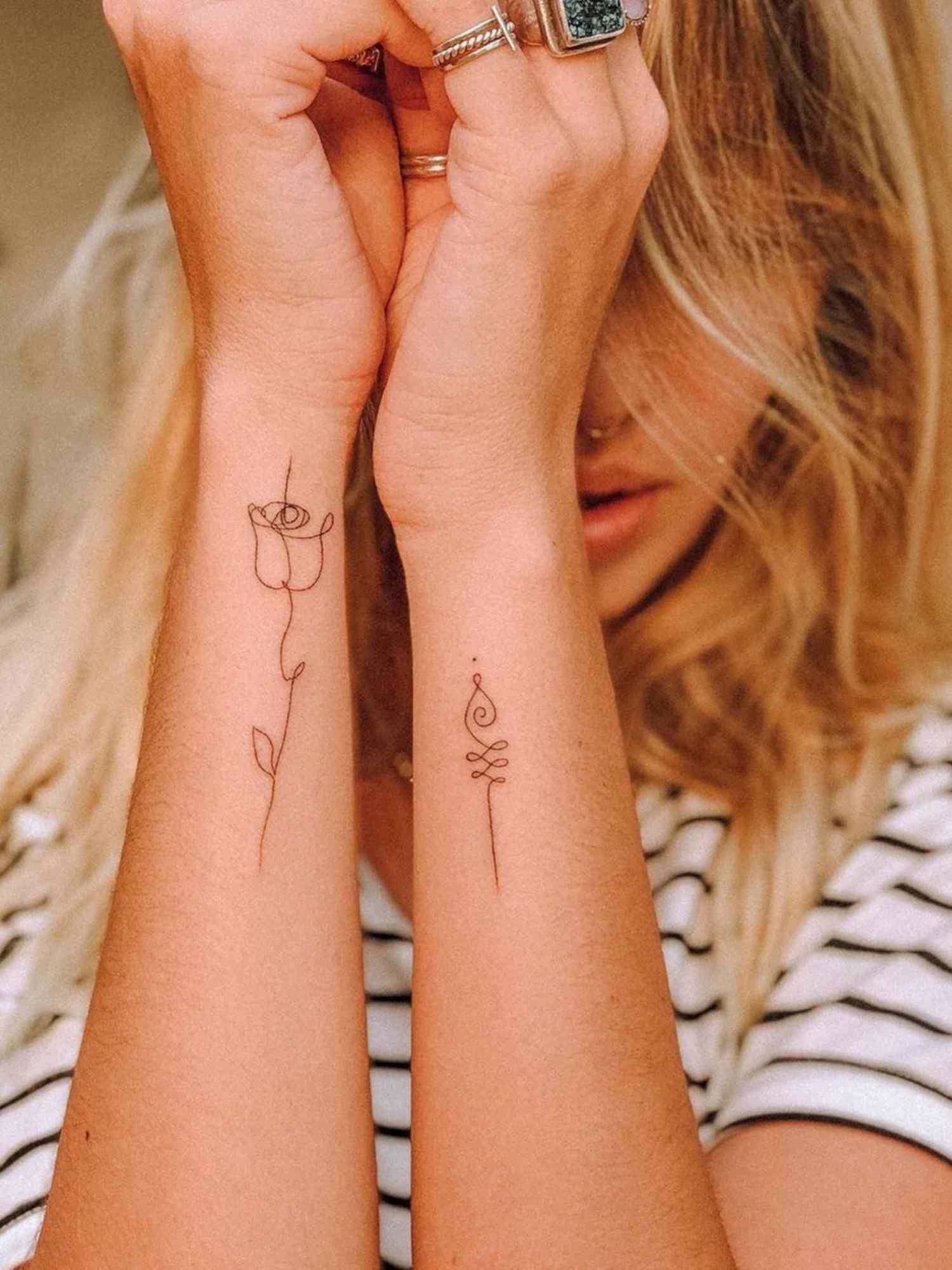 Delicate line work transforms these forearms into a garden of minimalist beauty, with a graceful rose bloom on one arm perfectly complemented by an elegant botanical flourish on the other. The matching placement creates stunning symmetry when the arms are brought together, while each tattoo stands beautifully on its own 🌹 Simple black ink proves that sometimes the most understated designs make the biggest impact.