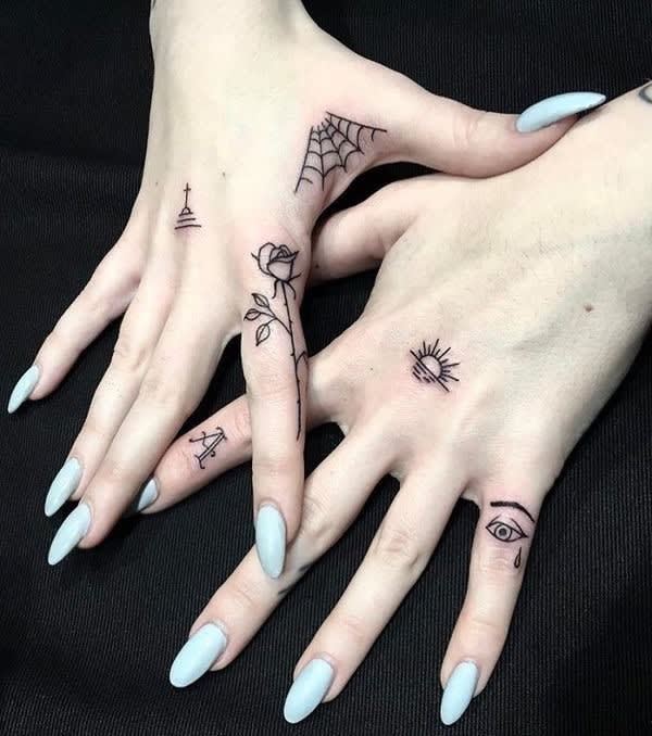 Delicate black ink transforms these hands into a canvas of mystical symbolism, featuring a spiderweb corner piece, blooming rose along the finger, and an all-seeing eye that adds an enchanting gothic touch. The minimalist line work creates perfect harmony between darkness and elegance, while the pale blue nails provide a stunning contrast that makes each tiny tattoo pop with personality. ✨