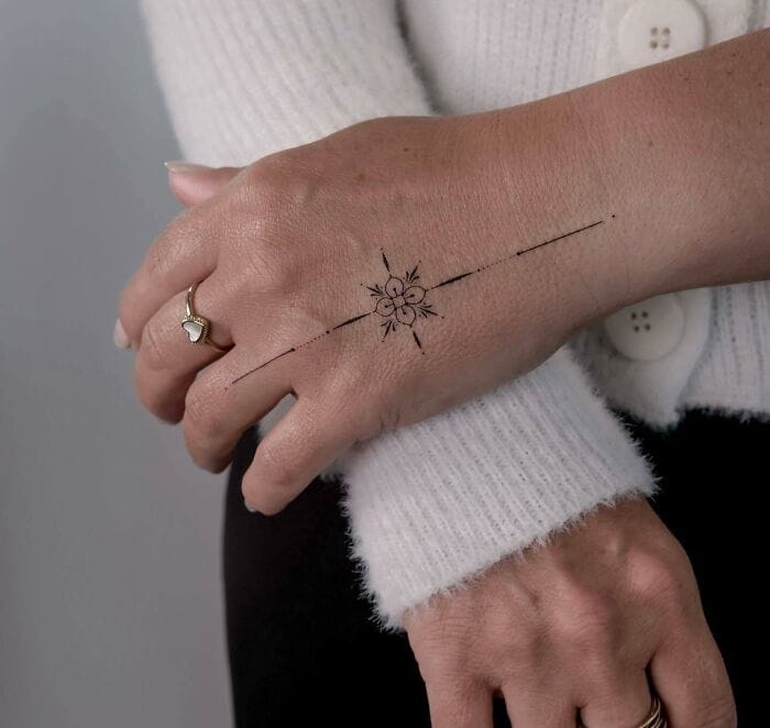 Delicate line work transforms this hand into a celestial canvas, where a radiant sun symbol anchors elegant rays that flow seamlessly across the skin. The minimalist black ink design creates an ethereal compass effect, perfectly complementing the hand's natural curves while making a subtle yet striking statement ✨