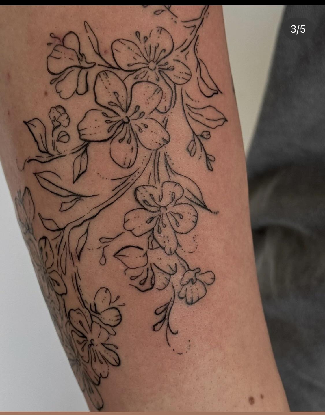 Cascading down the forearm like nature's own delicate masterpiece, this botanical line work showcases lilies in various stages of bloom connected by graceful flowing vines. The artist's precise dotwork technique adds incredible texture and depth to each petal, while the organic composition wraps beautifully around the arm's natural contours 🌸 Perfect inspiration for anyone seeking elegant floral ink with timeless black and grey sophistication.