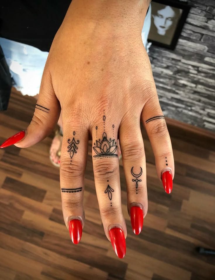 Delicate mandala motifs dance across each finger in this stunning hand tattoo, creating an intricate symphony of geometric patterns and mystical symbols. The ornate lotus design on the middle finger serves as a beautiful centerpiece, while crescent moons and decorative arrows flow seamlessly between the knuckles ✨ Bold red nails provide the perfect contrast to these fine-line black ink details, making this hand jewelry truly unforgettable.