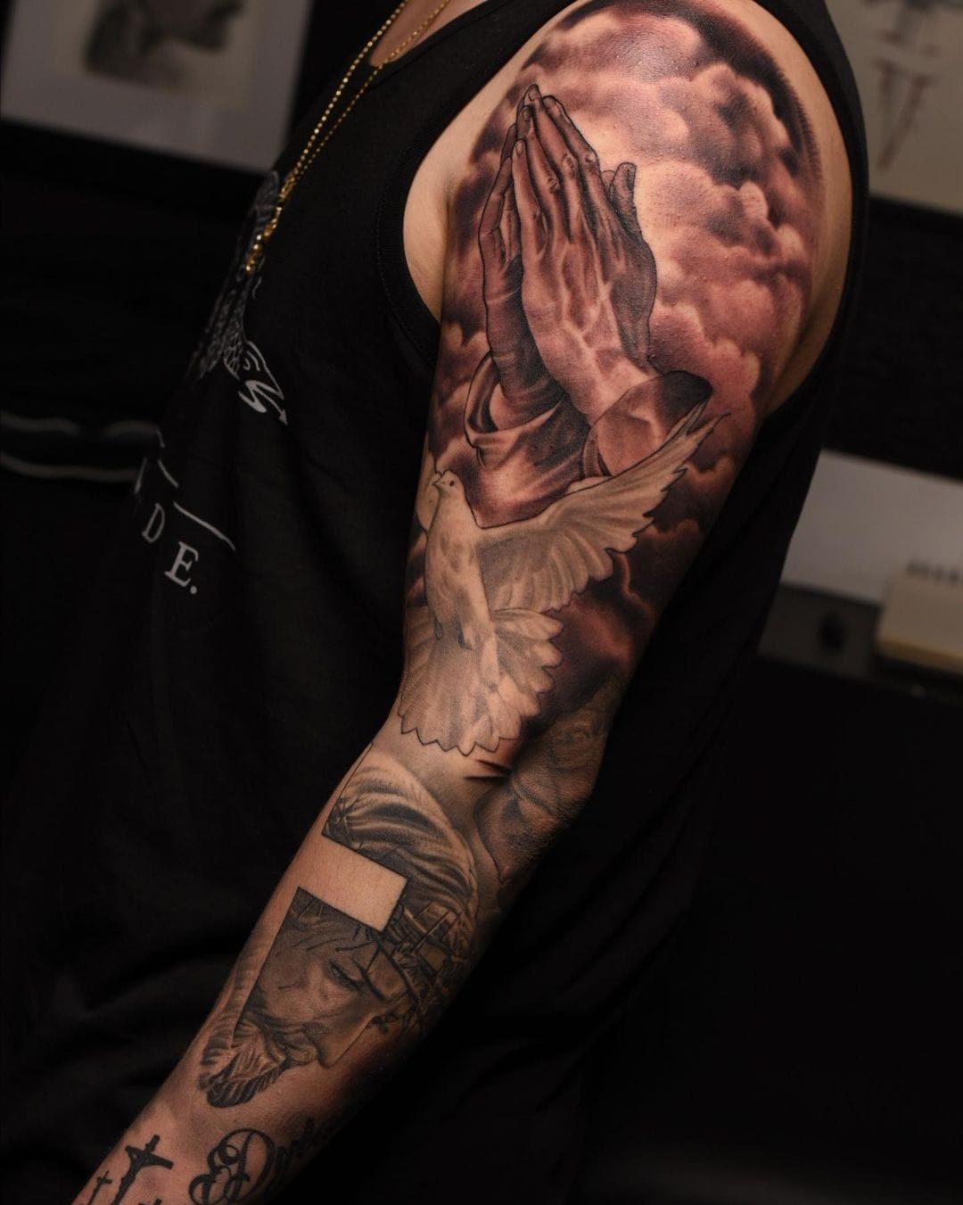 Praying hands reach toward heavenly clouds in this masterfully shaded religious sleeve, where divine wings unfold with breathtaking realism across the upper arm. The artist's exceptional use of black and gray creates dramatic depth, seamlessly blending spiritual symbolism with technical prowess that transforms skin into a canvas of faith. Every feather detail and shadow gradient speaks to both devotion and artistry 🙏