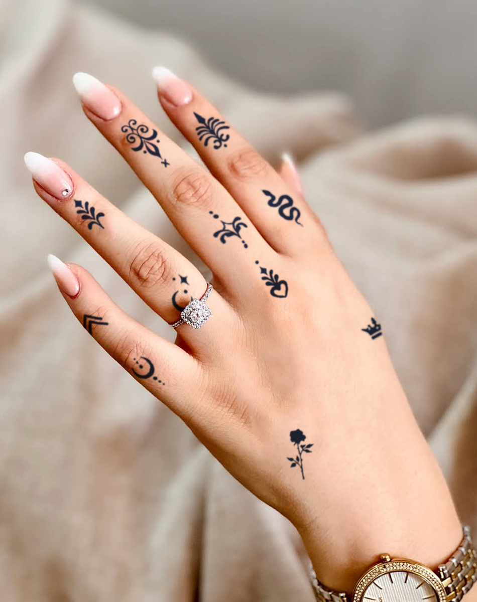 Delicate botanical motifs dance across fingers and cascade down the hand like a secret garden in miniature form. Each tiny black ink flourish - from ornate crosses to whimsical leaves - creates an enchanting tapestry that transforms everyday gestures into artful expressions. The contrast between the dainty designs and that stunning engagement ring makes this hand tattoo collection absolutely mesmerizing ✨