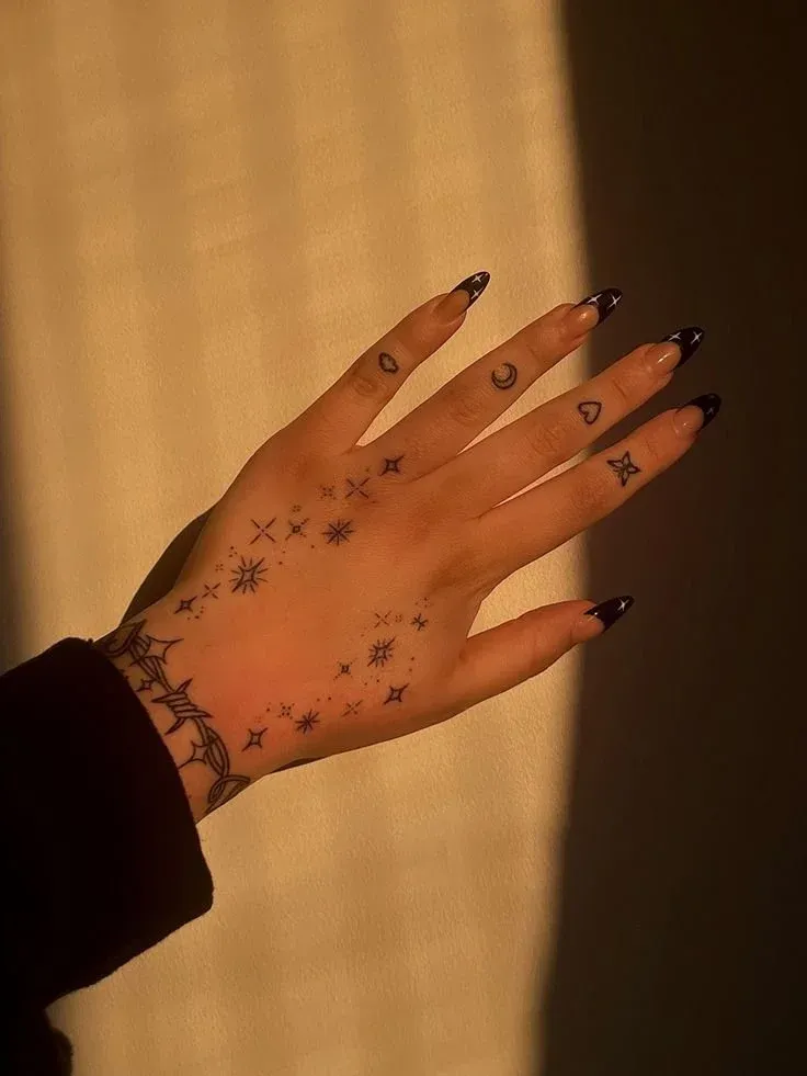 Delicate celestial magic dances across this hand in the most enchanting way ✨ The scattered stars, moons, and cosmic symbols create a dreamy constellation that flows naturally from wrist to fingertips, while that gorgeous barbed wire bracelet adds just the right edge to balance the ethereal vibes. Perfect for anyone who wants to carry a piece of the night sky with them wherever they go.