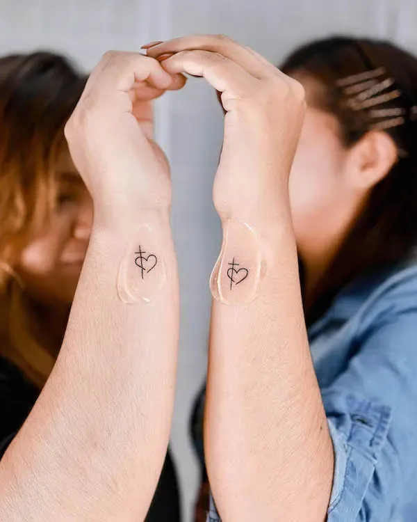 Delicate matching wrist tattoos featuring minimalist cross-heart symbols create an intimate bond between these two souls ✨ The clean linework and thoughtful placement on the inner wrists means these meaningful designs stay close to their pulse points, symbolizing faith and love flowing through their very being. When they join hands, the tattoos align perfectly—a beautiful reminder of their shared spiritual journey and connected hearts.