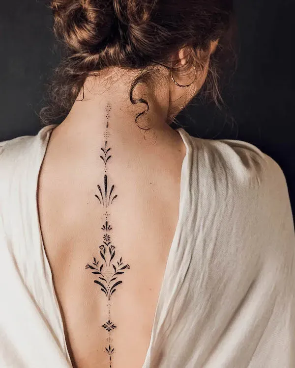 Delicate botanical elements cascade down the spine in this stunning vertical design, creating an enchanting garden that follows the natural curve of the back. The intricate line work features symmetrical florals and geometric accents that seem to bloom directly from the skin, while the strategic placement along the vertebrae adds an almost mystical quality to this nature-inspired masterpiece. 🌿