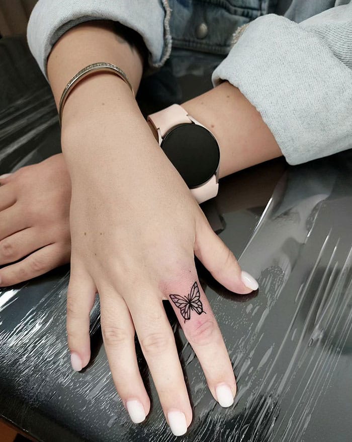 Delicate linework transforms this ring finger into a canvas for metamorphosis, with a minimalist butterfly that seems to flutter across the skin. The geometric wings create beautiful negative space, making this piece feel both bold and understated—perfect for someone who wants meaningful ink that whispers rather than shouts 🦋