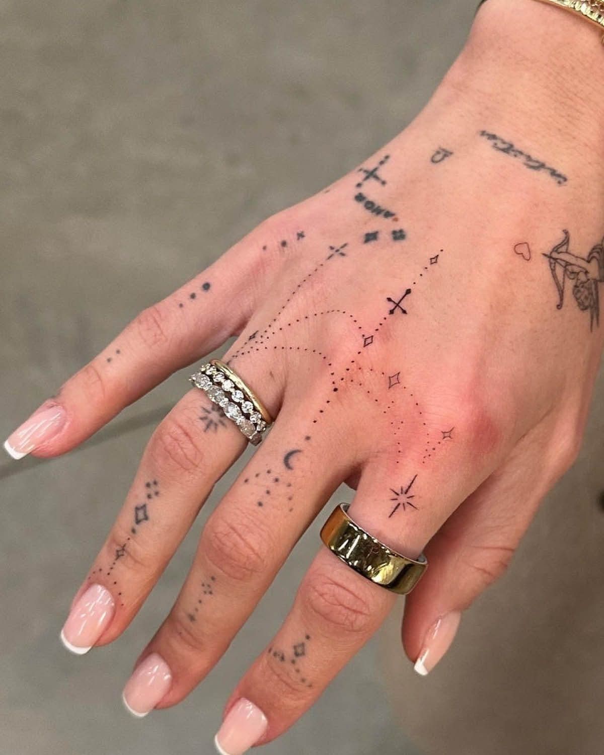 Delicate celestial magic unfolds across fingers and palm in this enchanting hand tattoo that transforms skin into a personal star map ✨ Dotted constellations, tiny crosses, crescent moons, and mystical symbols create an intricate cosmic landscape that's both bohemian and deeply meaningful. The fine line work and strategic placement make every gesture feel like casting spells with stardust.