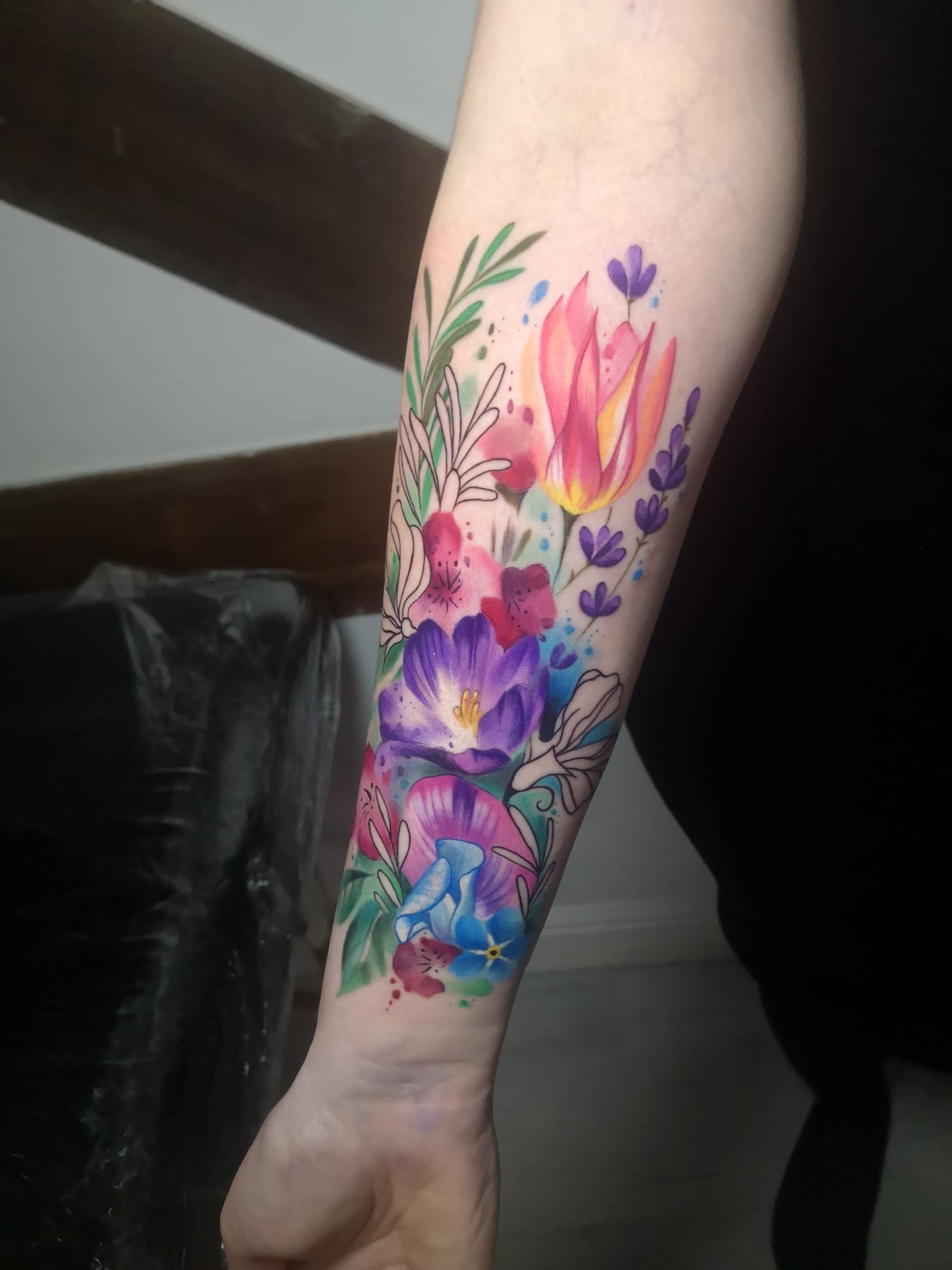 Watercolor magic blooms across this forearm in a stunning botanical symphony of pink tulips, purple crocuses, and delicate lavender sprigs 🌸 The artist's masterful use of color bleeding and splatter effects creates an almost painted-on-canvas illusion, while the strategic placement allows the floral arrangement to flow naturally with the arm's contours. This piece perfectly captures the ephemeral beauty of a spring garden in permanent ink.