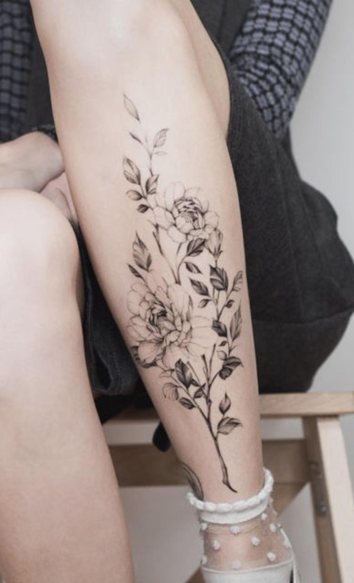 Delicate linework transforms this shin into a botanical garden, where graceful peonies bloom alongside trailing stems in perfect black ink harmony. The vertical placement elongates the leg beautifully while the fine-line technique creates an almost ethereal quality that looks like it was sketched by nature itself 🌸
