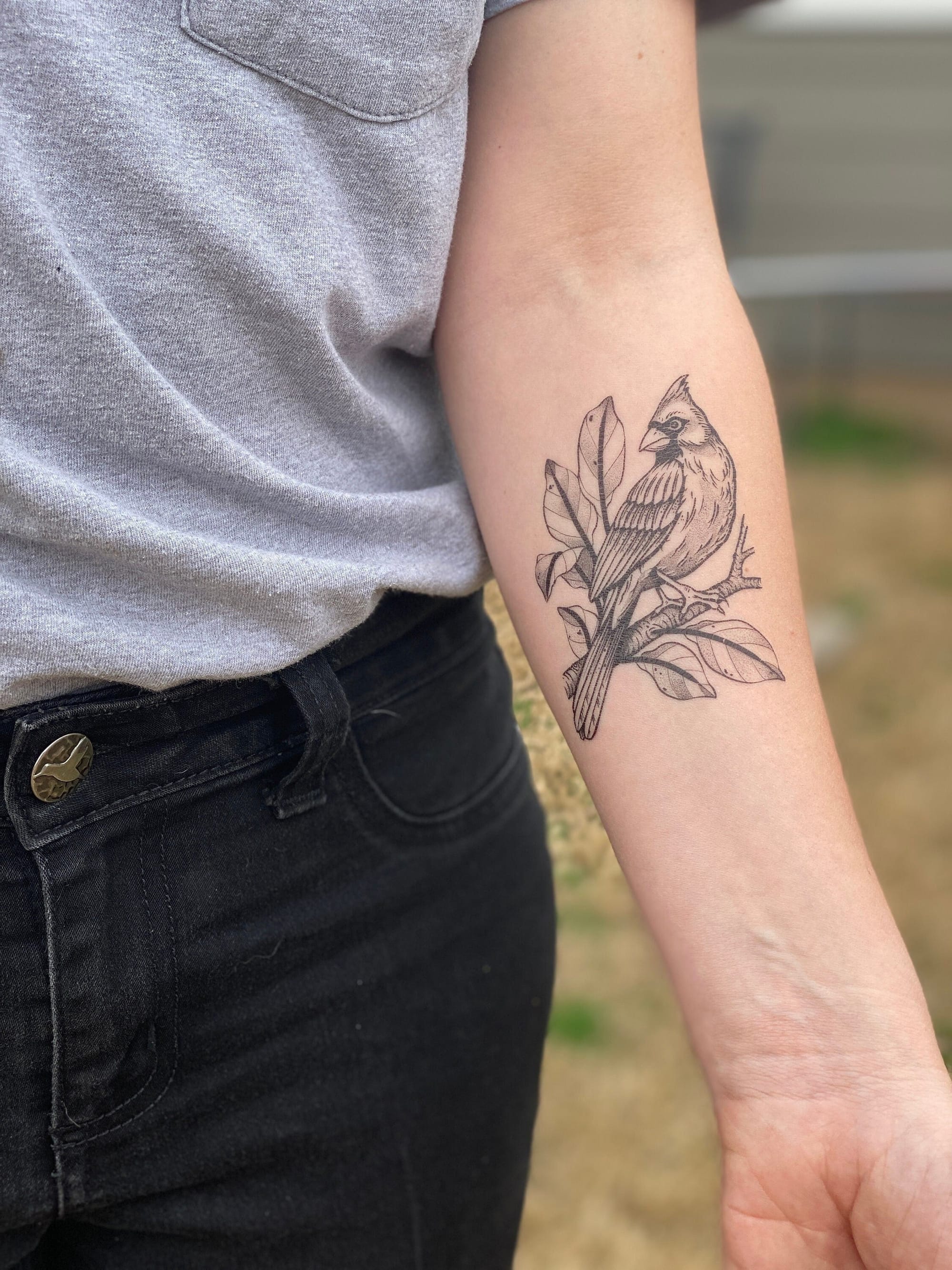Delicate linework brings this cardinal and botanical design to life on the forearm, where fine black ink captures every feather detail and leaf vein with stunning precision. The way the bird seems to naturally perch among the flowing foliage creates such an organic, harmonious composition that feels both timeless and deeply personal 🕊️