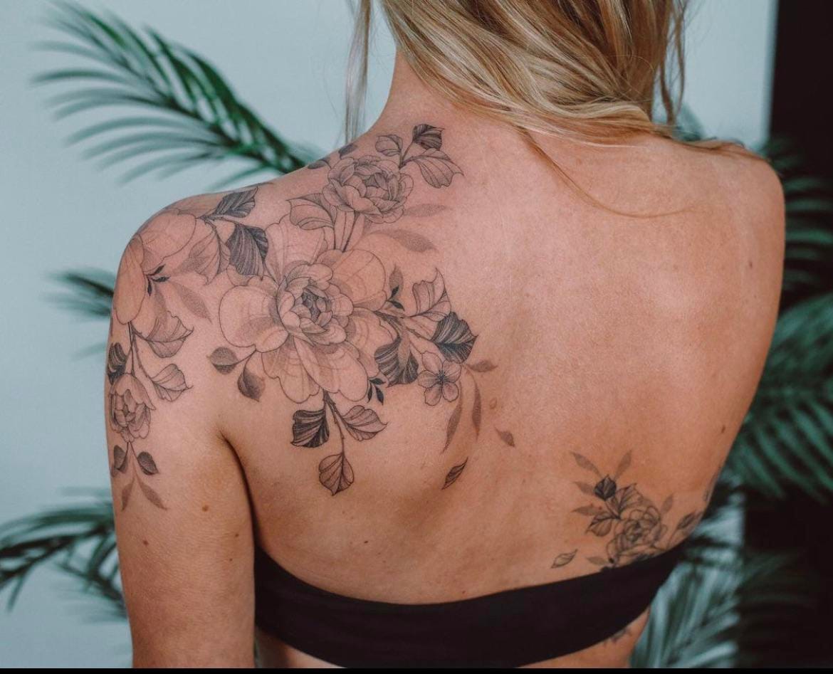 Cascading down her shoulder blade like nature's own masterpiece, this delicate floral composition features roses and botanical elements rendered in stunning black and grey linework. The organic flow of petals and leaves creates a beautiful symphony across her back, with smaller blooms echoing the design along her ribcage for perfect visual balance. 🌹