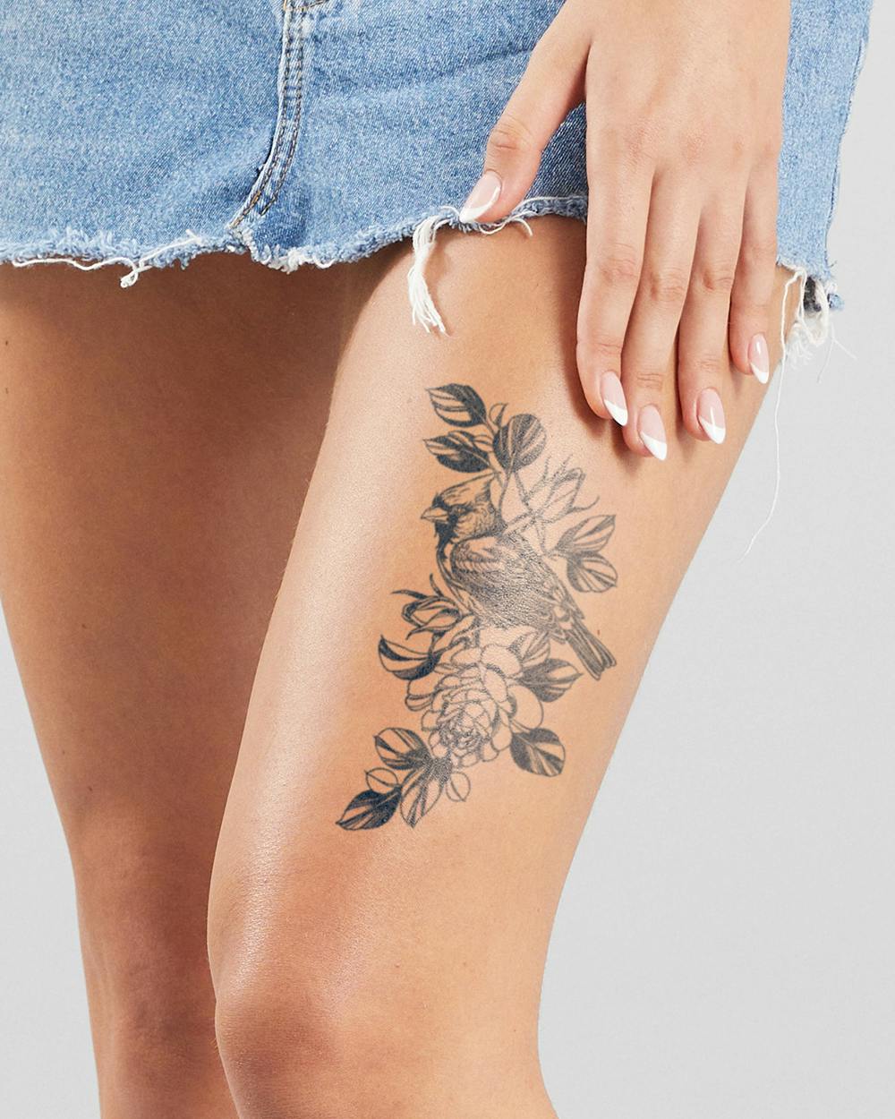 Delicate botanical artistry meets avian elegance in this stunning thigh piece, where a cardinal perches gracefully among blooming peonies and flowing foliage. The intricate line work creates beautiful depth and movement, transforming the upper leg into a canvas that celebrates nature's harmony. Perfect placement that allows the design to flow naturally with the body's curves while remaining beautifully framed by casual denim ✨