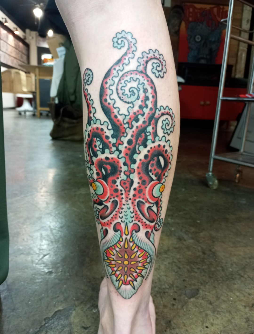 Bold traditional artistry meets oceanic mythology in this stunning leg piece featuring a vibrant red octopus with mesmerizing tentacle spirals. The intricate dotwork and classic tattoo palette create incredible depth, while the decorative mandala at the bottom adds a beautiful finishing touch that perfectly balances the composition 🐙