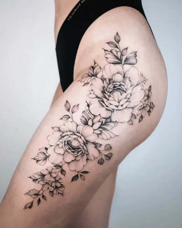 Cascading down the thigh like a botanical waterfall, this exquisite black and gray floral piece transforms the leg into a living canvas of delicate peonies and trailing foliage. The artist's masterful shading technique creates incredible depth and dimension, with each petal appearing to bloom naturally from the skin 🌸 The flowing composition follows the body's natural curves perfectly, making this placement both feminine and powerful.