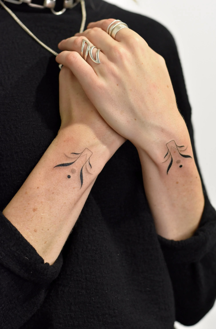 Delicate line work transforms these wrists into a canvas of ethereal beauty, where matching angel wing silhouettes create perfect symmetry across both arms. The minimalist black ink design features graceful feather details and subtle dots that add depth without overwhelming the clean aesthetic ✨ When positioned together like this, the wings appear to embrace the wearer in their own protective embrace.