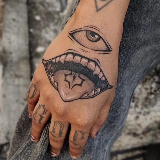 Bold linework transforms this hand into a mesmerizing canvas where surreal meets street art - an eye gazes outward while an open mouth reveals intricate inner details that blur the line between anatomical study and artistic expression. The strategic placement across knuckles and palm creates a dynamic piece that shifts and moves with every gesture, making the wearer's hand itself part of the storytelling. 👁️
