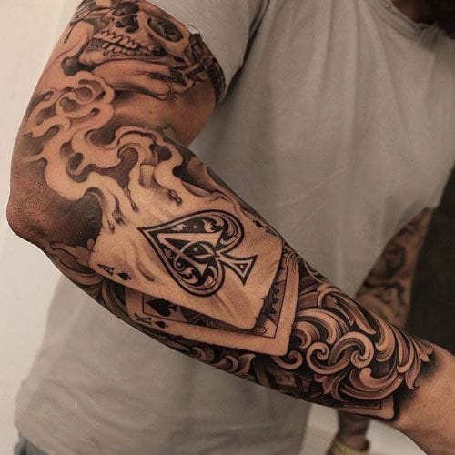 Intricate black and grey artistry transforms this entire forearm into a masterpiece of contrasts - delicate playing cards float among bold swirling clouds and ornate baroque details. The seamless blend of gambling symbolism with flowing organic elements creates a sleeve that's both edgy and elegantly refined ♠️
