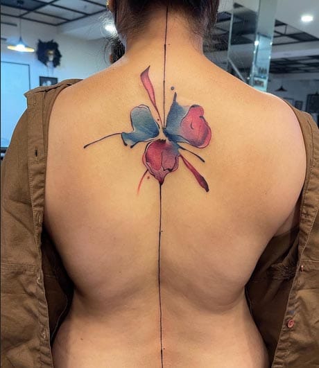 A delicate butterfly emerges along the spine's natural line, its wings painted in soft watercolor washes of coral pink and dusty blue that seem to float effortlessly across the skin. The artist's masterful use of negative space and flowing brushstroke techniques creates an almost ethereal quality, as if this beautiful creature just landed for a moment before continuing its graceful flight 🦋