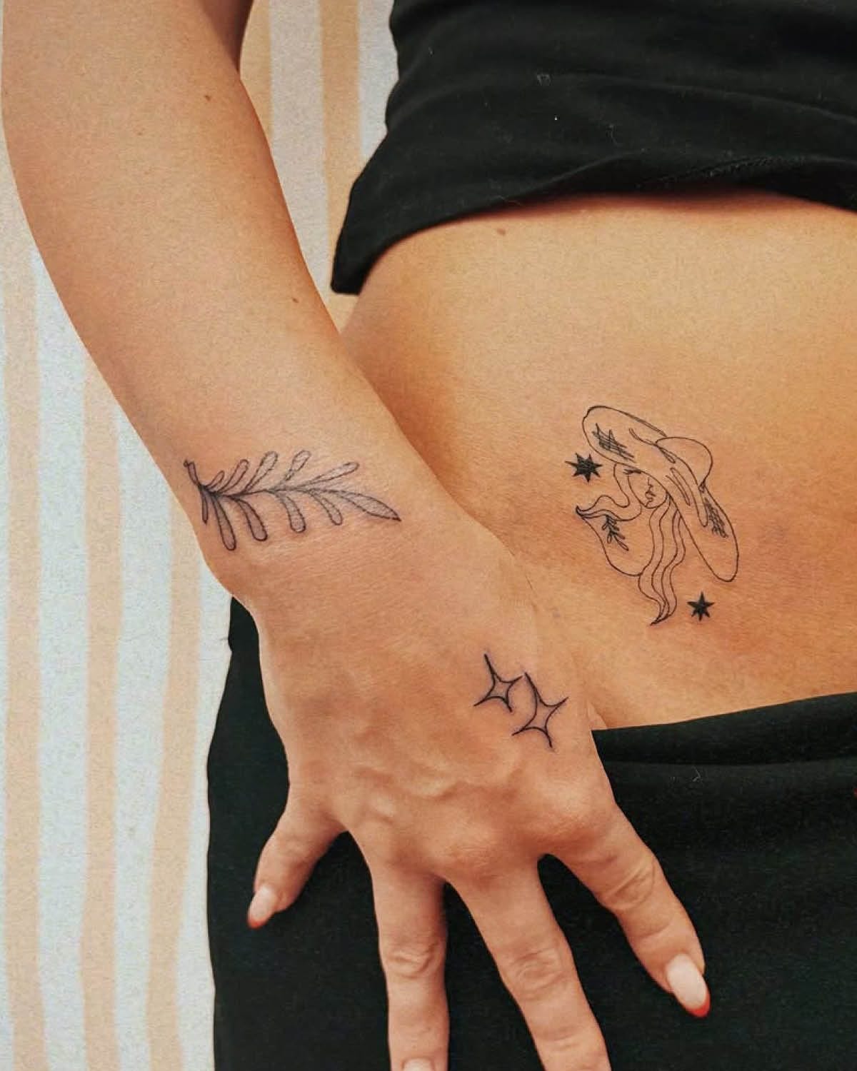 Delicate line work transforms skin into a botanical dreamscape, featuring a graceful fern frond on the forearm that perfectly complements the mystical cowgirl silhouette adorned with stars on the ribcage. The minimalist hand tattoo of interconnected stars creates a stunning trinity of ink that flows seamlessly across the body's natural curves. ✨