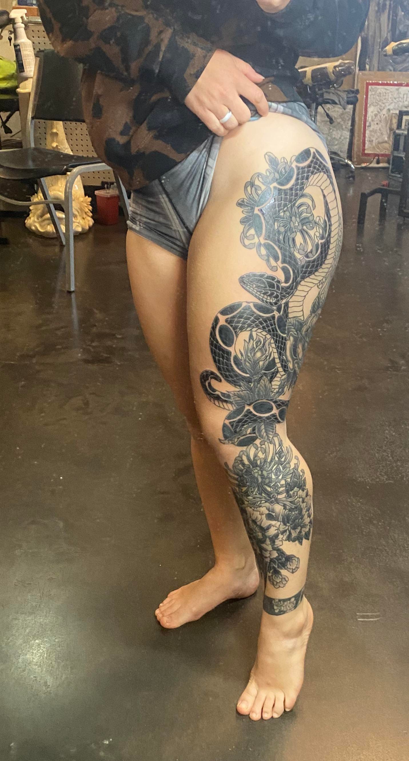 A serpentine masterpiece winds its way from thigh to ankle in this breathtaking Japanese-inspired leg sleeve, where dragons dance through clouds and chrysanthemums bloom in eternal ink. The intricate shading and bold linework create a stunning contrast against skin, transforming this leg into a living canvas that tells an ancient story of power and beauty. 🐉 The seamless flow from hip to foot showcases how expert tattooing can turn the human body into pure art.