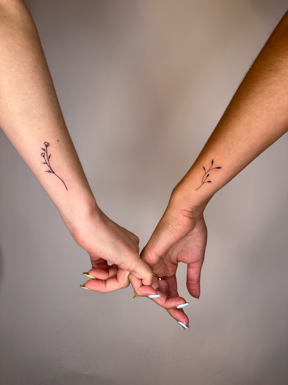 Delicate botanical sprigs bloom across these intertwined wrists, creating a stunning matching tattoo set that celebrates connection through nature's simplicity. The minimalist line work features graceful stems with tiny leaves and buds, positioned perfectly to mirror each other when hands come together 🌿 A beautiful symbol of growth, partnership, and the organic bonds that tie us to those we love.