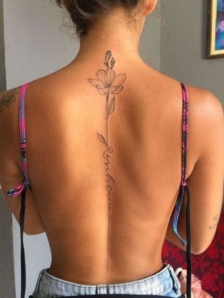 Delicate linework transforms the spine into a botanical masterpiece, where an elegant rose bloom crowns a graceful stem that follows the natural curve of the vertebrae. The minimalist script woven into the design adds an intimate touch to this stunning back piece that perfectly complements the body's anatomy. 🌹
