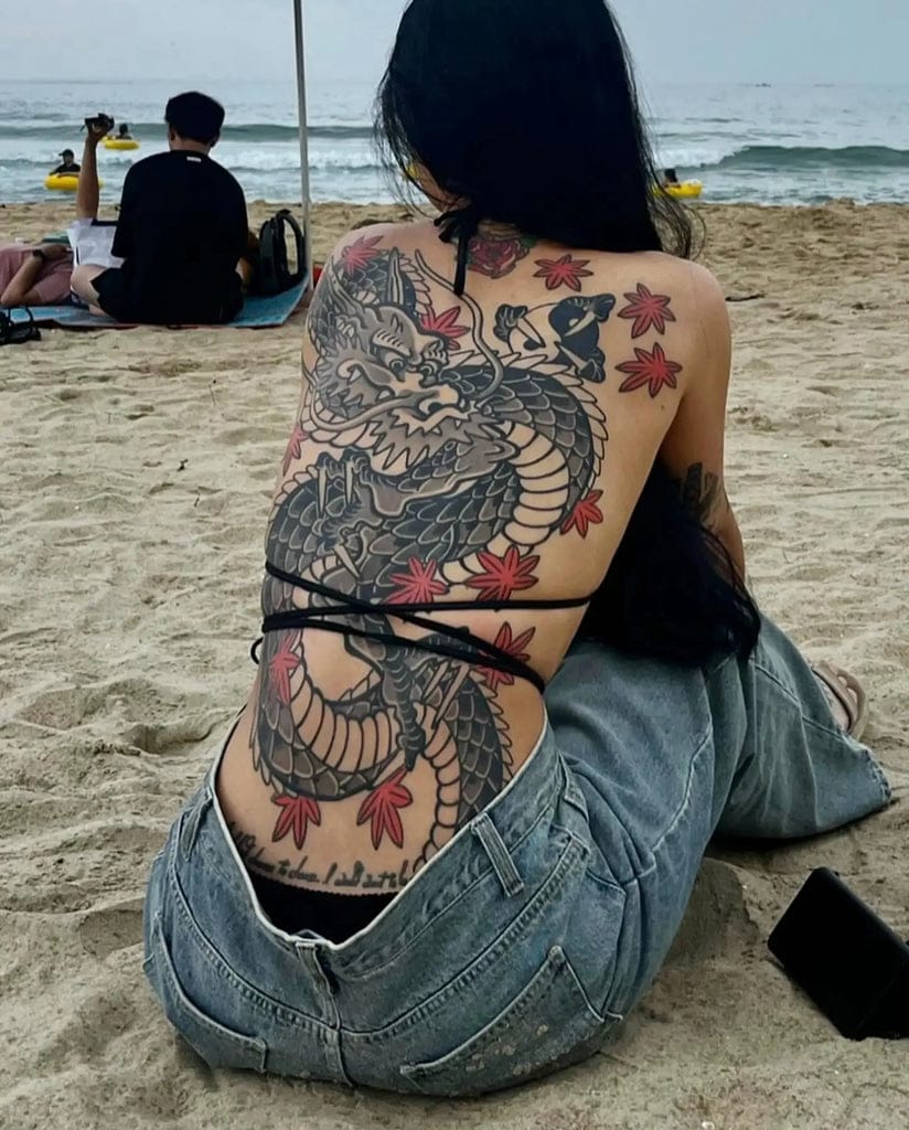 Serpentine power flows across this breathtaking back piece, where an intricately detailed dragon coils from shoulders to lower back amid delicate cherry blossoms. The masterful contrast between the bold black scales and soft pink petals creates a stunning Japanese-inspired composition that transforms the entire torso into living art. Beach vibes meet ancient mythology in this show-stopping full back masterpiece 🐉
