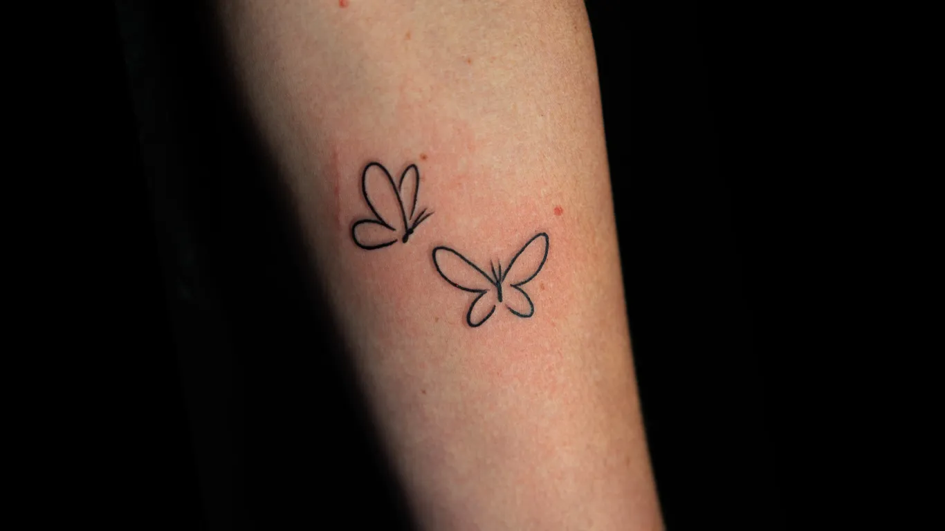 Delicate line work brings two butterflies to life on this minimalist forearm piece, where simplicity meets profound symbolism. The clean, unshaded outlines create an almost sketch-like quality that feels both timeless and contemporary—perfect for someone who appreciates understated elegance with deep meaning. 🦋