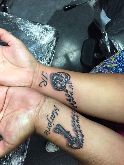 Two hands unite to reveal a meaningful connection through matching lock and key tattoos, with delicate chain details that flow seamlessly across the wrists. The intimate placement and complementary design create a beautiful symbol of partnership, where one person literally holds the key to unlock the other's heart 🔐