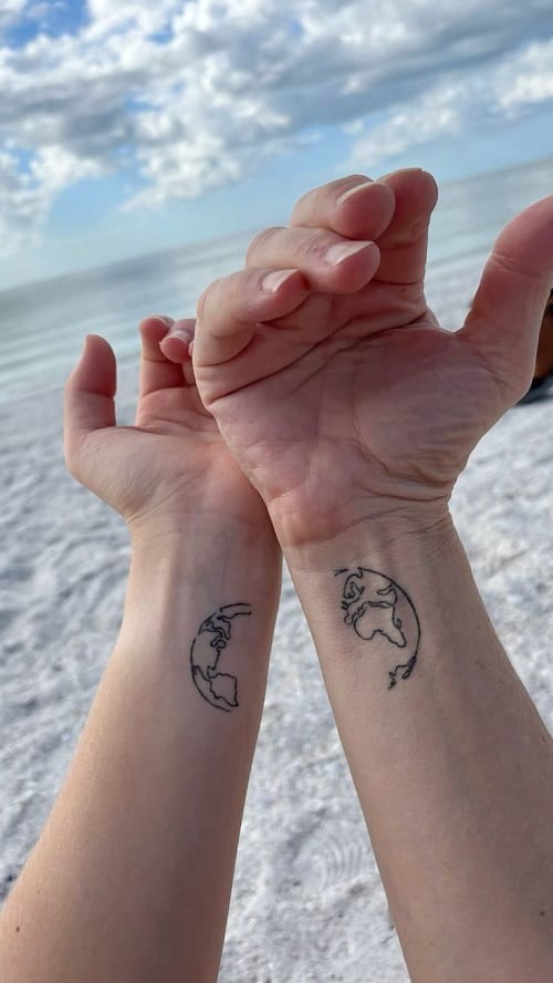 Two souls, two worlds, forever intertwined on matching wrists that tell a story of connection across continents 🌍 The minimalist line work captures Earth's delicate beauty in perfect halves, creating a stunning visual metaphor when these hands come together. Set against the pristine beach backdrop, these complementary tattoos prove that the most meaningful ink doesn't need color to make a powerful statement.