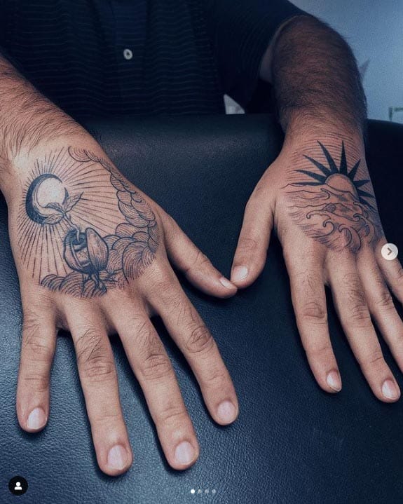 Celestial forces collide across these striking hand tattoos, where moon and sun engage in an eternal cosmic dance ☀️🌙 The left hand showcases intricate linework featuring a crescent moon surrounded by radiating beams and mystical details, while the right displays a bold sun with flowing rays that seem to move with every gesture. Perfect placement for someone who carries the balance of day and night wherever they go.