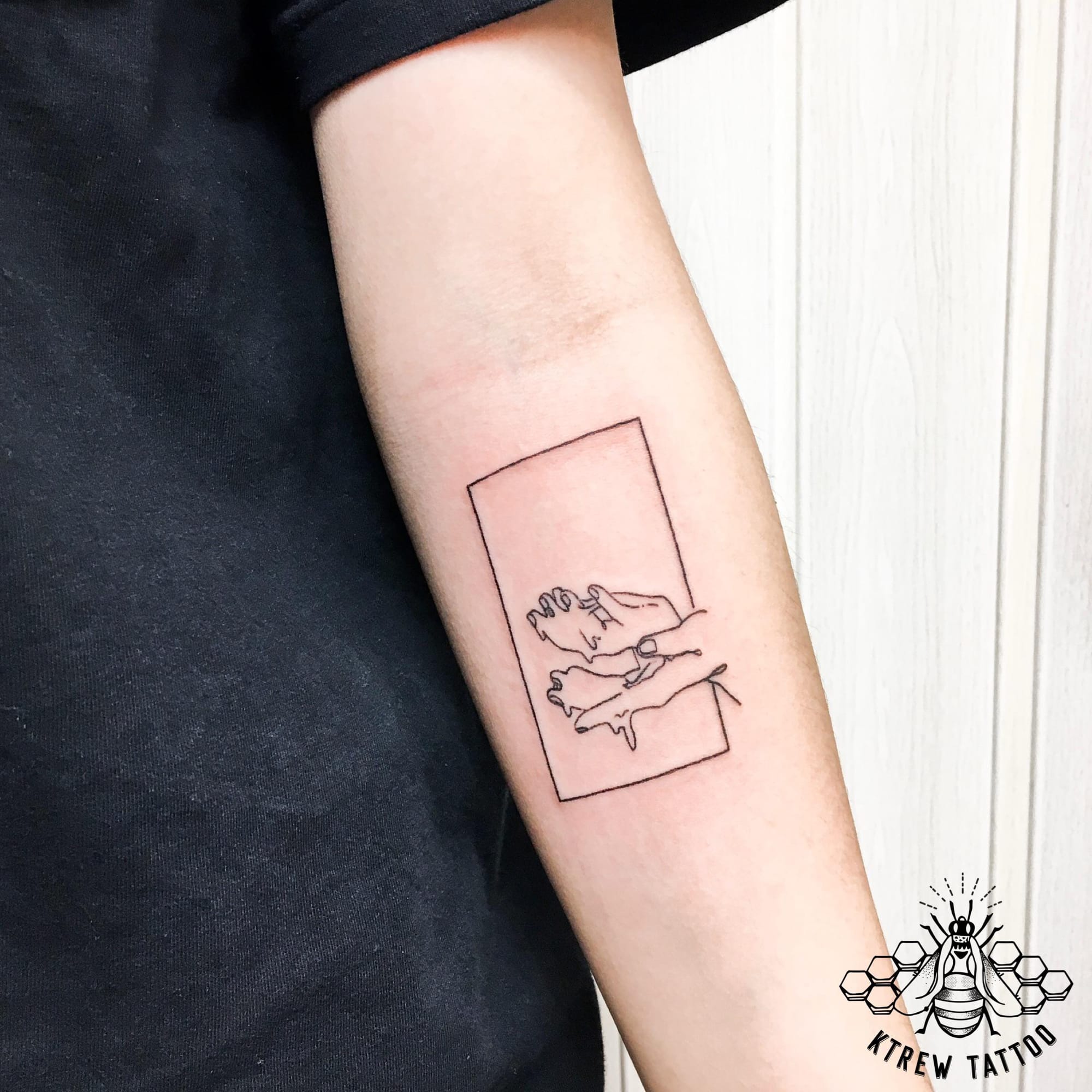 Fine line artistry meets playful romance in this minimalist forearm piece, where delicate linework captures an intimate moment within a perfectly squared frame. The simple geometric border transforms the design into a living polaroid, creating a timeless snapshot that feels both personal and universally relatable 📸