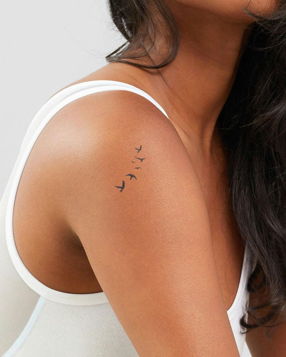 A delicate flock of birds takes flight across this shoulder blade, creating a minimalist masterpiece that speaks to wanderlust and freedom. The simple black silhouettes follow the natural curve of the body, making this placement both elegant and symbolic ✨ Perfect for those who dream of soaring above life's limitations.
