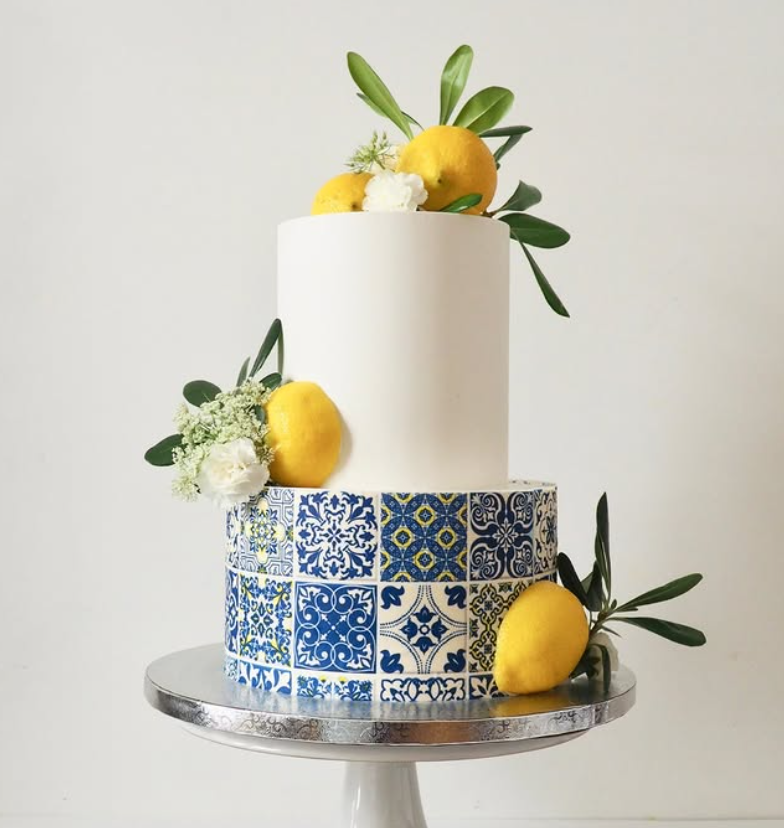 Two-tier buttercream wedding cake with fresh greenery on a restaurant table set for a 40-guest reception.