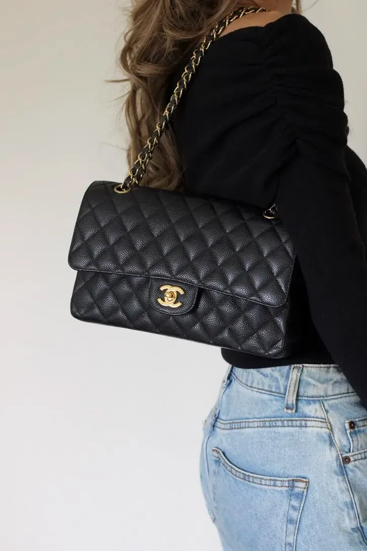 同一款 Chanel Classic Flap,只係由金扣轉做銀扣,整體氣質已經可以好唔同。圖中為金扣 black caviar(黑色牛皮荔枝紋)配黑色上衣及牛仔褲嘅日常上身效果,但整體仍然帶有較強 Dressy Casual 感覺。